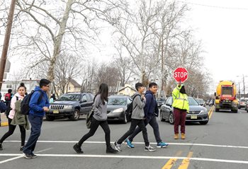 A crossing guard holds up a stop sign to stop cars while children cross the street.